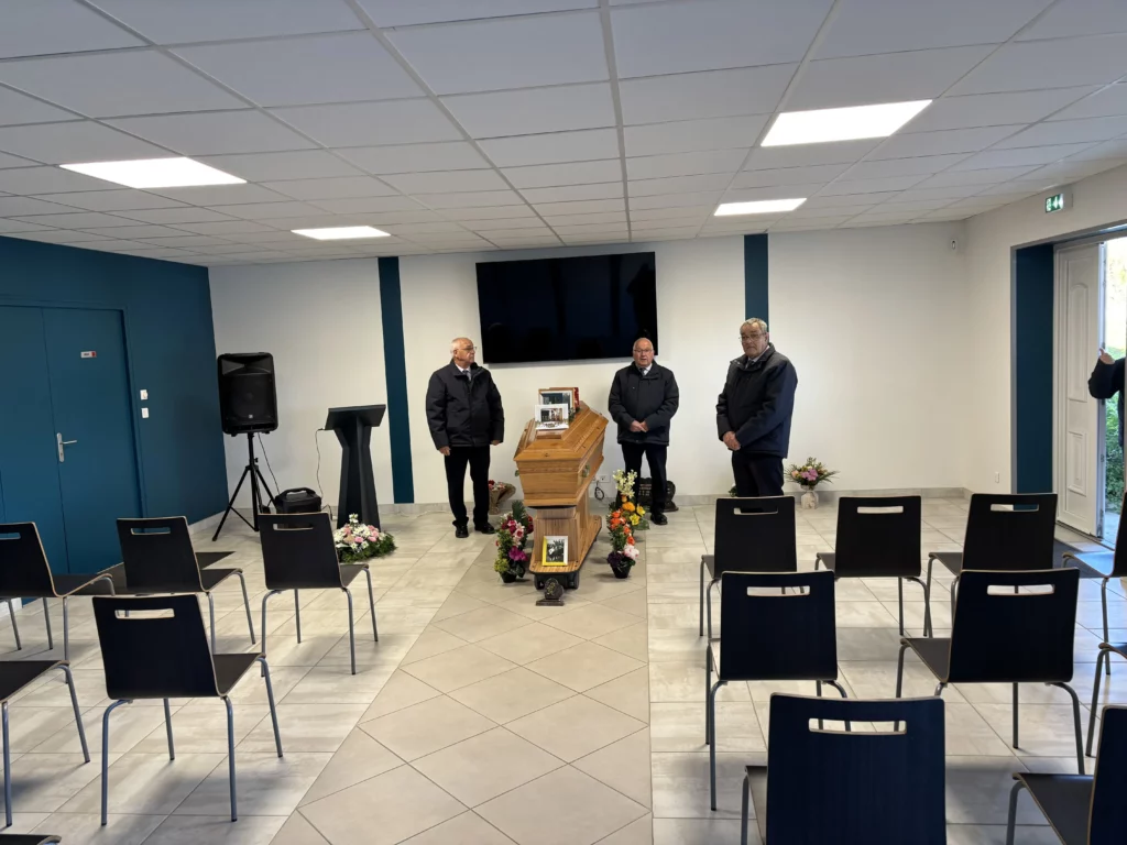 Salle de cérémonie funéraire aménagée avec un cercueil en bois et des chaises.