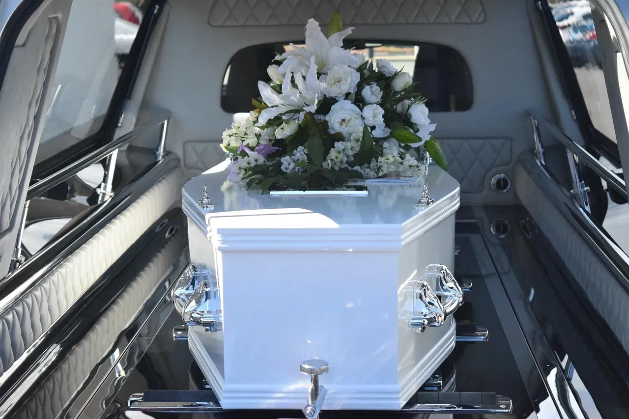 Cercueil blanc recouvert d'un bouquet de lys dans un corbillard de transport.